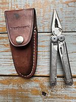 Leatherman Wave multitool closed with leather sheath placed on wooden surface.