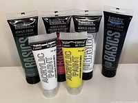 Five acrylic paint tubes from Liquitex Basics and Water Colour brands, colors green, black, dark gray, white, and yellow, tubes shown upright and full.
