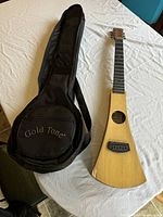 Photo of Martin & Co Backpacker acoustic guitar next to black Gold Tone branded soft case on a white surface.