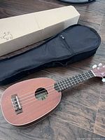 Ukulele, soft carry case and original box displayed on wooden floor.