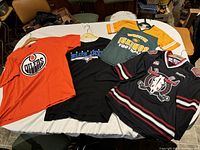 Photo showing all four items: Red Deer Rebels WHL black jersey, orange Edmonton Oilers shirt, green Edmonton Eskimos jersey, and black Toronto Blue Jays shirt
