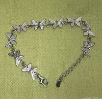 Top-down view of a sterling silver butterfly bracelet arranged in a loose heart shape on a green fabric background.