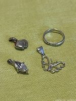 Top view of all four items: heart pendant, marquise stone pendant, butterfly pendant, and ring with 'FAITH' engraving laid flat on yellow fabric.