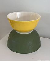 Two Pyrex mixing bowls stacked upside down - yellow bowl on top, green bowl underneath, showing exterior color and shape