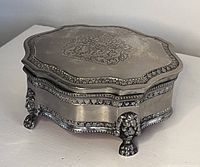 Angled view of the silver plated jewelry box showing the engraved British Royal Crest on the lid and lion-footed base with decorative trim.