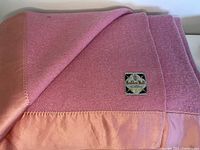 Close-up showing the pink wool blanket with satin trim and Haddon Hall label.