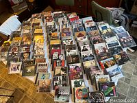 Wide overview of a large collection of classic rock CD jewel cases spread out on a table showing diverse album covers and artists.