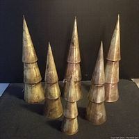 Six brass metal trees shown against a black backdrop, varying heights and stacked conical shape.