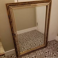 Full view of vintage framed wall mirror leaning against wall on patterned floor.