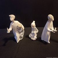 Three NAO by Lladro porcelain figurines of children in nightshirts, positioned on a black surface with a dark background.