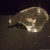Clear glass bear sculpture resting on a black surface, viewed from the right side showing embedded fish detail.
