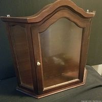 Closed view of the small wooden curio cabinet showing the glass door and wooden frame with knob.