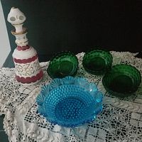 Overall lot showing decanter with stopper, three green hobnail bowls, one blue hobnail bowl on lace cloth