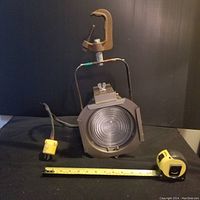 Front view of the vintage studio light on a black cloth background with yellow measuring tape showing width approximately 7 inches and height approximately 10 inches.