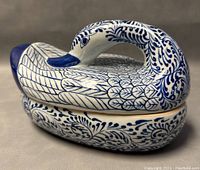Side view of the swan-shaped ceramic box highlighting the curved neck handle and intricate blue feather and foliage patterning.