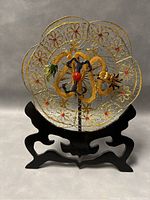 Front view showing the detailed gold-tone filigree work, enameled dragon centerpiece, and black wooden stand.