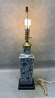Front view of the vintage blue and white porcelain lamp on black base, showing floral pattern and lit bulb in brass fixture.