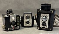 Three vintage Kodak Brownie cameras: Hawkeye Flash #620, Hawkeye camera, and Brownie Rebel in case.