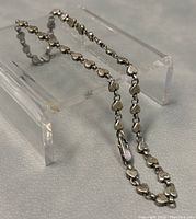 Full view of silver heart link choker necklace laid out on a display stand.