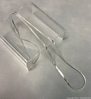 22 inch sterling silver necklace displayed on a clear acrylic stand on a grey textured background, showing the chain length and flat reflective design.