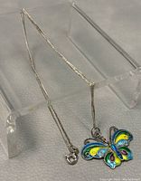 Photo showing full silver chain with butterfly pendant suspended on clear stand, displaying chain details and clasp.