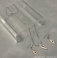 Necklace and matching earrings displayed on clear stand showing leaf-shaped silver pendants with stones.