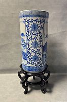 Front view of the blue and white ceramic umbrella stand on its wooden base showing detailed scenic floral and landscape patterns.