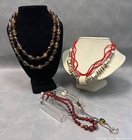 Group photo of three costume necklaces on black and white neck displays and clear stand