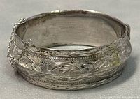 Front view showing etched floral, leaf and geometric patterns and safety chain on hinged sterling silver bangle.