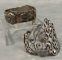 Two silver bangles including a hinged and a cuff bracelet displayed on a clear acrylic stand