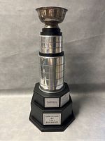 Front view of large silver road hockey cup trophy with engraved plaques and black base.