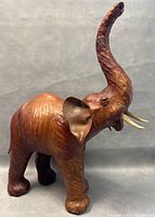 Front-side view of the elephant statue with raised trunk, visible glass eyes, tusks, and leather texture.