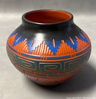 Front view of the handcrafted Navajo pottery pot showing painted and etched geometric designs in orange, blue, and black.