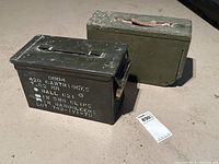 Two WW2 military boxes side by side on the ground, showing worn surfaces and details distinguishing them as ammunition and equipment storage boxes.