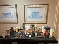 Photo showing the candle lot with a variety of pillar candles, votive candles, tealight packs, taper candles, and decorative candle holders arranged on a black countertop under two framed architectural prints.