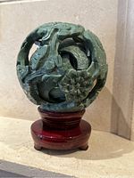 Full view of the carved jade sphere sculpture on lacquered wooden base, showing floral and dragon motifs.