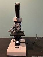 Front view of electric microscope showing stage, objective lenses, eyepiece and power switch with power cord attached.