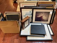 Photo showing large framed art pieces including an abstract photographic art print with a light color palette, smaller framed art with blue graphic elements, and several flat stacked frames.