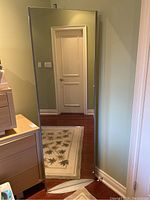 Front view of full-length rectangular mirror with silver frame reflecting a door and part of the room.