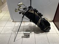 Side angle showing the golf clubs in the stand bag with legs deployed and box containing golf ball monogram stamper in front