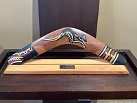 Full view of boomerang mounted on wooden stand showing the shape and painted design.