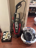 Husky 1800 PSI power washer standing upright with hose wrapped around it. Two containers on either side holding various cables, power strips, and electronic accessories.
