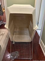 Photo showing the assembled large plastic dog crate with metal door open and hardware bag in front. Beige crate with ventilation slots.