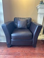 Front view of dark brown leather armchair with down-filled back cushion and matching throw pillow, showing mark on right arm.