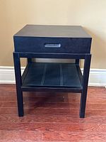 Front angled view of black side table showing drawer and lower shelf with white lines.