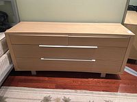Front view of a modern blond wood dresser with four drawers and chrome handles.