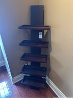 Shelf viewed at an angle showing five horizontal tray-like wooden shelves mounted on a vertical support, dark finish.