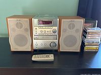 Full view of Sony stereo system with two wooden speakers on each side, remote control in front, and stack of cassette tapes to the right.