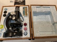 Overview photo of Tasco 900 microscope and accessories in foam case with wooden hinged top open