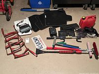 Multiple vehicle accessories including floor mats, gas can, stereo receiver, ratchet straps, and vehicle cleaning tools laid out on a concrete floor for condition and content display.